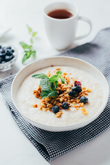 close-up on a plate with oatmeal, banana, mint berries on a background of dishes on a white table