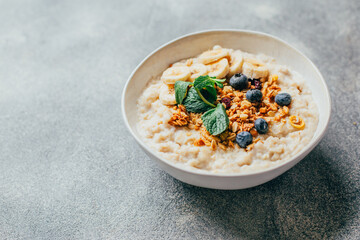 close-up on a plate with porridge fruits berries nuts and mint on a grey table