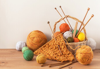 Winter crafts. Process of hand knitting warm bright scarf for cold season. Knitting supplies, set of colorful wool balls in wicker basket, wooden knitting needles and hooks on table. Knitting as hobby