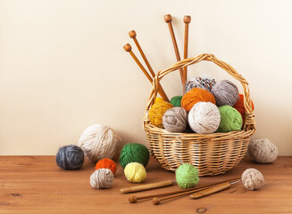 Wool clews of warm soft wool yarn in wicker basket with wooden knitting needles and crochet hook on wooden table. Rustic still life. Needlework, hobbies and knitting. DIY concept. Closeup, copy space - obrazy, fototapety, plakaty