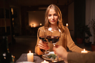 Happy young couple in love drinking wine clinking glasses celebrating Valentine's day dining at home with candles together