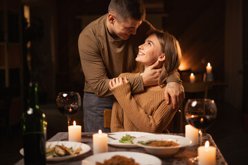Beautiful passionate couple having a romantic candlelight dinner celebrating Valentines Day at home, kissing.