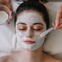 Beautician's hands applying clay face mask on caucasian woman face. Aesthetic procedure.