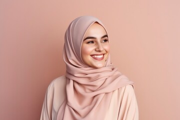 Happy joyful Muslim woman. A beautiful young girl in pink hijab smiles on plain pink background. Portrait of an Arab beauty with makeup in traditional clothes, human emotions