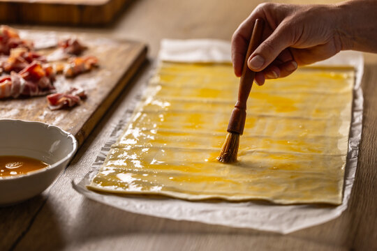 A female cook brushes puff pastry with egg