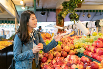 Asian woman buying fruit in a grocery store asks the clerk to help choose sweet and juicy fruit to...