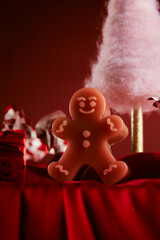 a figurine of a gingerbread man stands on a red silk tablecloth against the background of a pink felt tree and Christmas red candies, Christmas decorations, New Year decorations, close up view