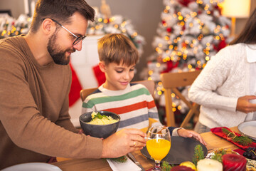 Father putting food on son's plate while having family Christmas dinner