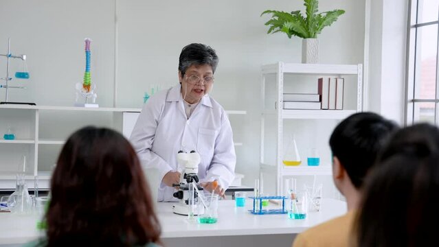 Elderly teacher teaches student about microscopy experiment, student sat intently looking at endoscopy so that would have do it himself later when teacher walks out does experiment for friends see.