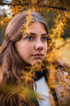Portrait of teenage girl standing in yellow autumn larch trees in the forest.