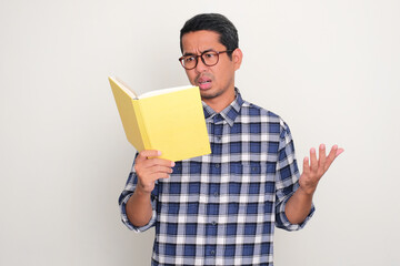 Adult Asian man reading a book with shocked expression