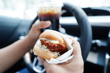 Asian woman driver hold and eat hamburger in car, dangerous and risk an accident.