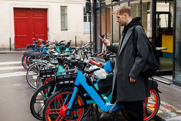 Young man unlocks bicycle with his mobile phone. Electric bicycle new way city mobility. Green...