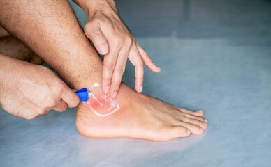 Man's hand is applying painkiller to his ankle due to pain, ankle inflammation, sprained ankle,...