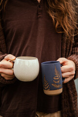 man with long hair holding two ceramic mugs full of coffee