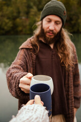 Man with long hair drinking coffee in nature by the river