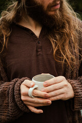Man with long hair drinking coffee in nature by the river