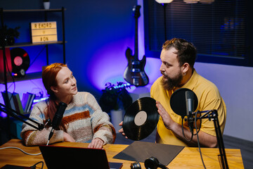 A radio presenter talks to a guest in the studio. A male blogger with a vinyl record in his hands...