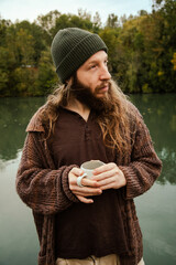 Man with long hair drinking coffee in nature by the river
