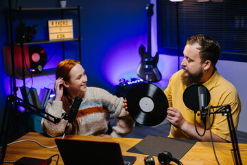 A radio presenter talks to a guest in the studio. A male blogger with a vinyl record in his hands...