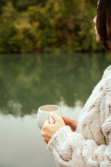 woman holding a cup of coffee close to her heart by the river