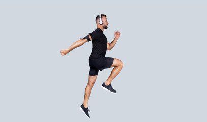 Focused young caucasian guy in wireless headphones, sportswear listen music, run, jump, freeze in air