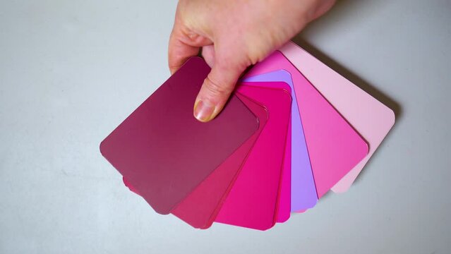 The hand of the adult spreads colored cards of red shades on the table.
