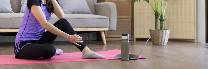 Woman looking at yoga teacher on laptop and doing light exercise in the living room at home, Watch live teaching or VDO on laptop, Dumbbells and a protein shake or bottle of water, Healthy exercise.