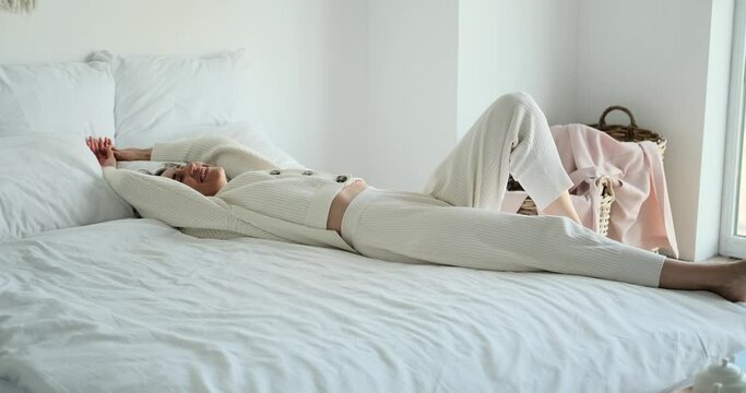 Carefree moment as a Caucasian woman joyfully tumbles onto bed in the bedroom. Her playful abandon and laughter fill the room, capturing a lighthearted and carefree atmosphere.