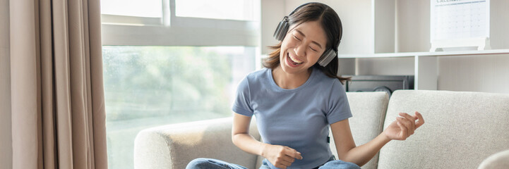 Fototapeta premium Young Asian woman happily listening to music through headphones, Woman was enjoying listening to her favorite music and rocking to the beat of the music, Stress relief, Happiness in life.
