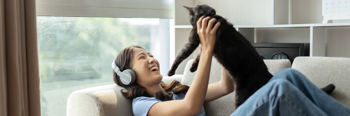 Young woman relaxing on sofa with her adorable black American Shorthair cat happily, Owner's...