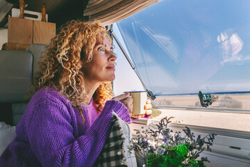 Serene adult woman admiring nature beach sitting inside a modern camper van in travel holiday...