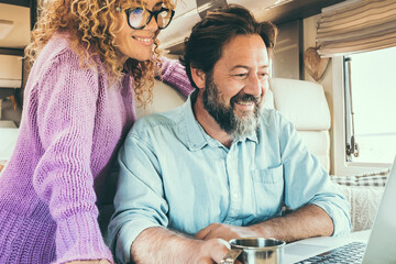Modern travel couple enjoy connection technology using laptop inside a camper van home. Alternative...