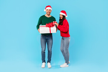 Young couple with Santa hats holding wrapped gift boxes, studio
