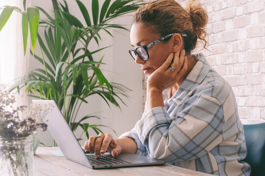 Concentrated professional freelance woman using laptop at home in office work place. People and digital smart working online job business occupation. Female write on computer with worried expression