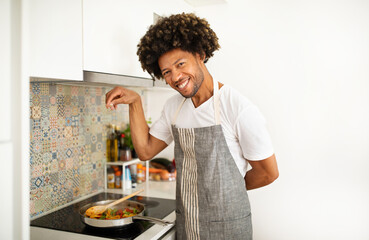 African American guy seasons a vegetable stew at modern kitchen