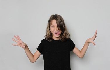 Surprise girl emotions. Surprised and happy child, arms to the sides, twisted face, tongue out, isolated on a light studio background.