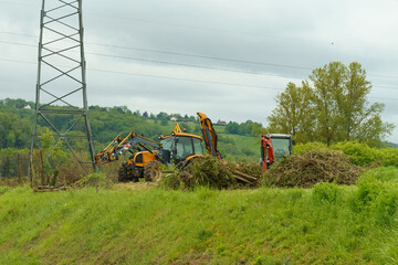 Tractors with brush cutters stand along the road on a hill behind cut bushes.