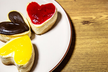 colorful cheesecakes heart shaped lemon chocolate and raspberry on white plate on wooden background closeup 