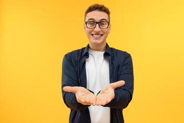 Cheerful young guy in eyeglasses showing something on his palms