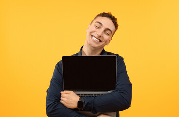 Joyful young guy hugging open laptop, yellow background