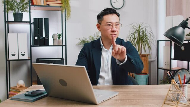 Asian middle-aged businessman working on laptop computer shakes finger and saying No be careful scolding giving advice to avoid danger mistake disapproval sign at home office. Confident freelancer man
