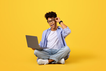 Cheerful black male student with laptop sitting cross-legged