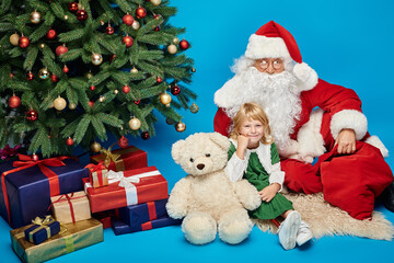 Fototapeta na wymiar happy child with prosthetic leg and teddy bear sitting with Santa Claus next to Christmas tree