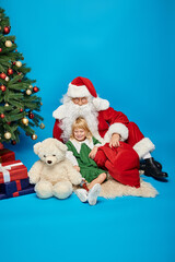 happy girl with prosthetic leg and teddy bear and sitting with Santa Claus next to Christmas tree