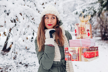 Excited woman holding heap of Christmas presents gift boxes in snowy winter park outdoors. Festive holiday season