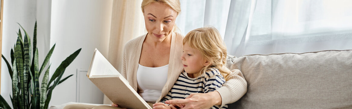 blonde mother reading book to daughter while sitting together in modern living room, banner