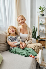 happy mother hugging daughter with prosthetic leg and sitting together on couch in living room