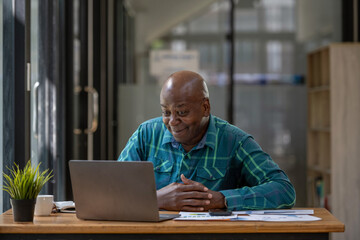 Fototapeta na wymiar A senior black man in casual clothes is taking a break from paperwork. Using a laptop to make video calls.