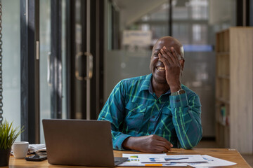 A senior black man in casual clothes is taking a break from paperwork. Using a laptop to make video calls